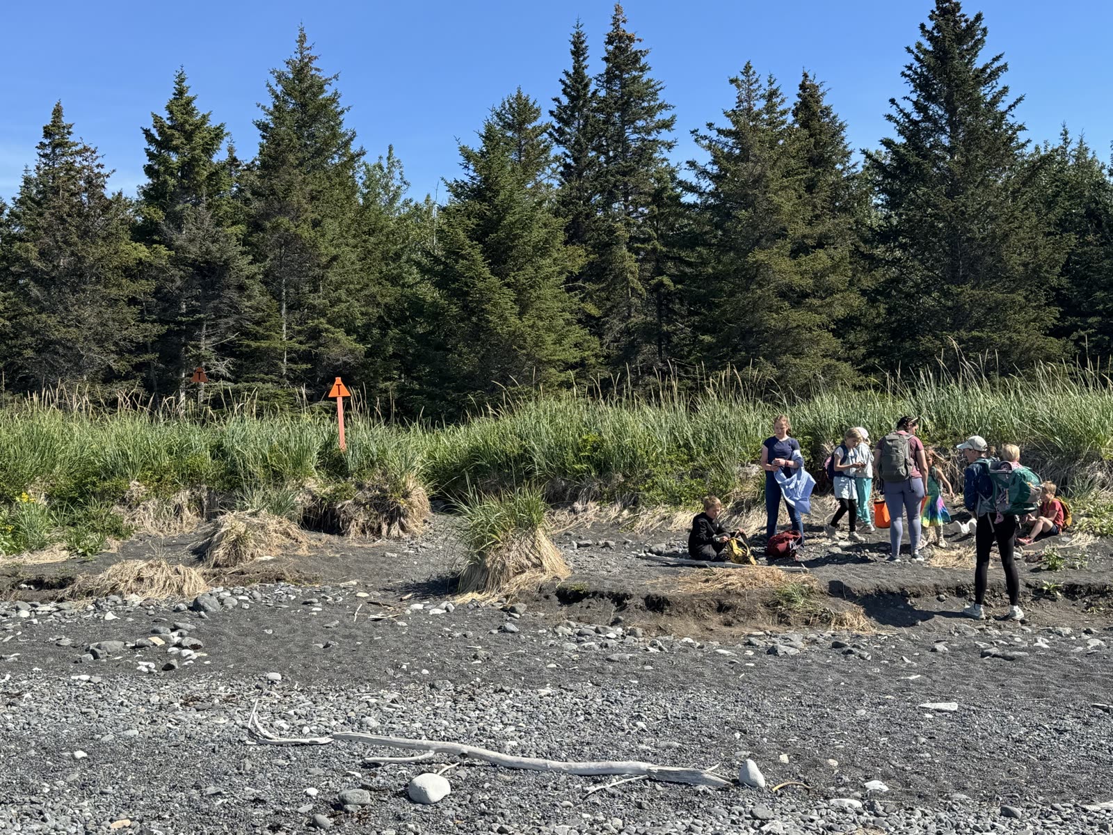 Group of hikers at the Glacier Spit trailhead with orange trail marker, Kachemak Bay State Park